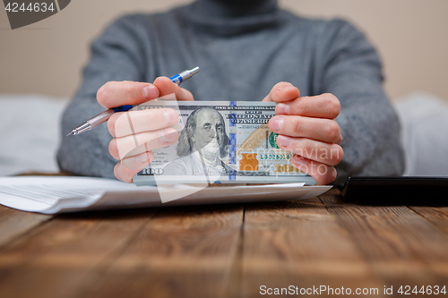 Image of Caucasian hands counting dollar banknotes on dark wooden table