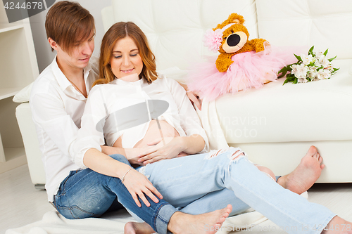 Image of man and a pregnant woman are sitting on the floor