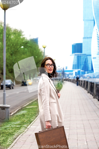 Image of beautiful business woman in a light coat with a stylish wooden c