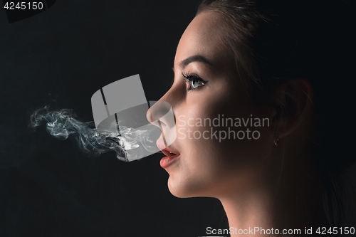 Image of The face of vaping young woman at black studio