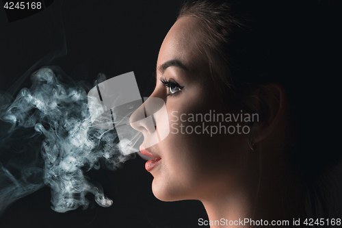 Image of The face of vaping young woman at black studio