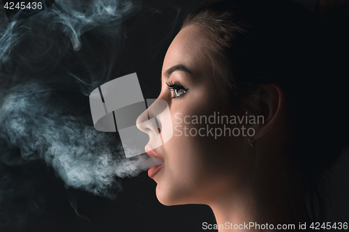 Image of The face of vaping young woman at black studio