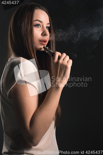 Image of The face of vaping young woman at black studio