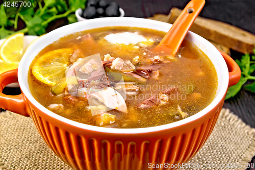 Image of Solyanka with lemon and spoon in bowl on board