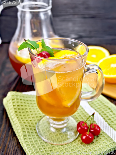 Image of Lemonade with cherries in wineglass and jug on dark board