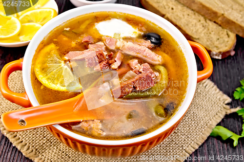 Image of Solyanka with lemon and black olives in bowl on board