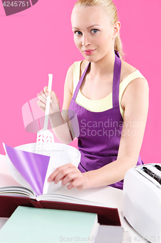 Image of Young, attractive housewife cooks food in a pink kitchen 