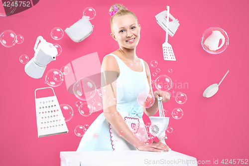 Image of Young, attractive housewife cooks food in a pink kitchen 