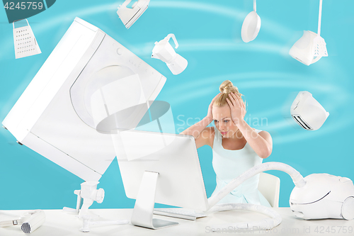 Image of Purchasing power vertigo - online shopping . A woman sits in front of a computer monitor and fly above it everyday appliances 