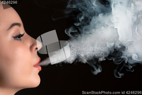 Image of The face of vaping young woman at black studio