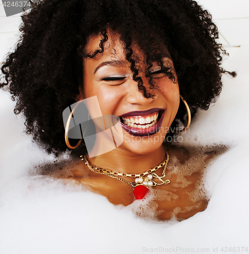 Image of young afro-american teen girl laying in bath with foam, wearing 