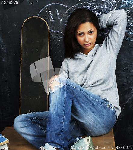 Image of young cute teenage girl in classroom at blackboard seating on ta