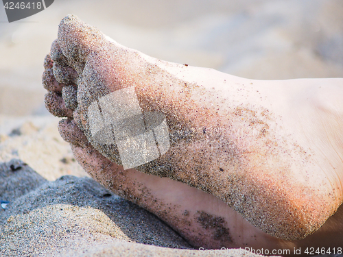 Image of Feet of one unrecognizable caucasian person resting in sand, wit