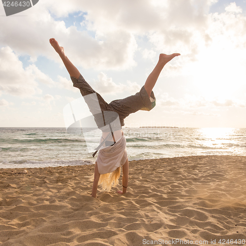 Image of Free Happy Woman Turning Cartwheel Enjoying Sunset on Sandy Beach.