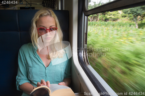 Image of Blonde caucasian woman reading book on train by the window.