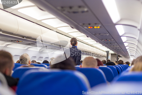 Image of Stewardess walking the aisle of commercial airplane.