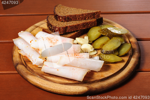 Image of Wooden plate with smoked bacon, pickles and rye bread