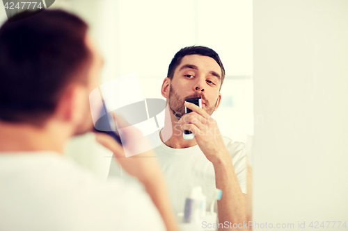 Image of man shaving mustache with trimmer at bathroom