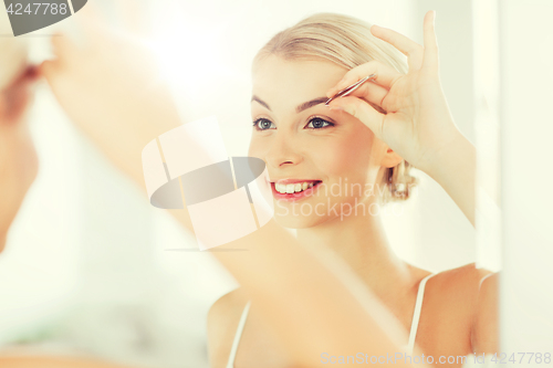 Image of woman with tweezers tweezing eyebrow at bathroom