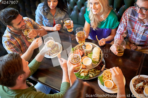 Image of happy friends eating and drinking at bar or pub