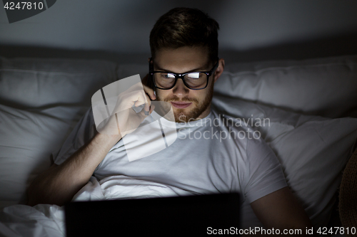 Image of man with laptop calling on smartphone at night