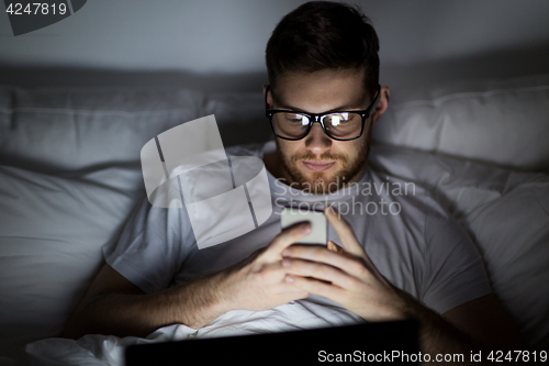 Image of man with laptop and smartphone at night in bed