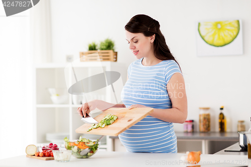 Image of pregnant woman cooking vegetable salad at home