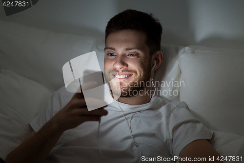 Image of man with smartphone and earphones in bed at night