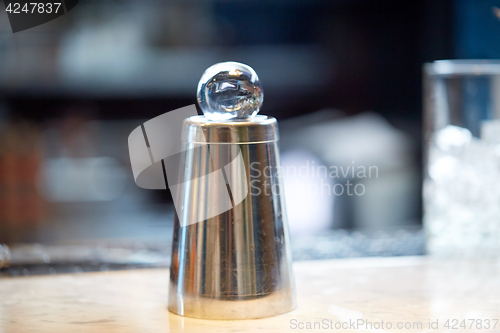 Image of hand-cut ice ball on top of cocktail shaker at bar