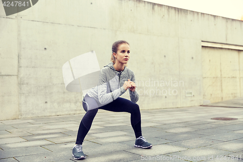 Image of happy woman doing squats and exercising outdoors