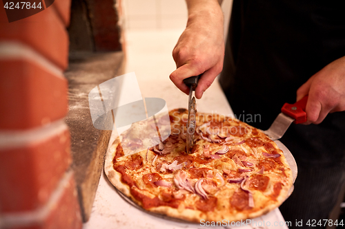 Image of cook hands cutting pizza to pieces at pizzeria