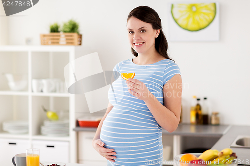 Image of happy pregnant woman eating orange at home