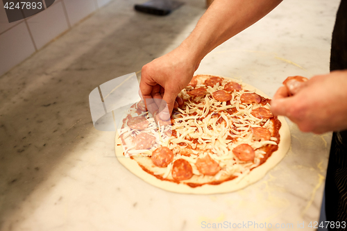 Image of cook hands adding salami to pizza at pizzeria