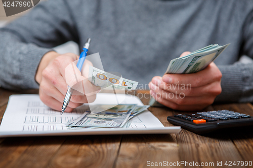 Image of Caucasian hands counting dollar banknotes on dark wooden table