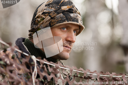 Image of hunter looks out from behind camouflage netting