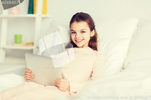 Image of happy girl lying in bed with tablet pc at home