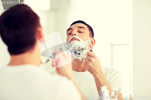 Image of man shaving beard with razor blade at bathroom