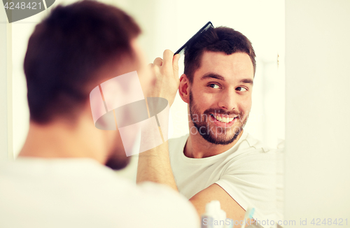 Image of happy man brushing hair  with comb at bathroom