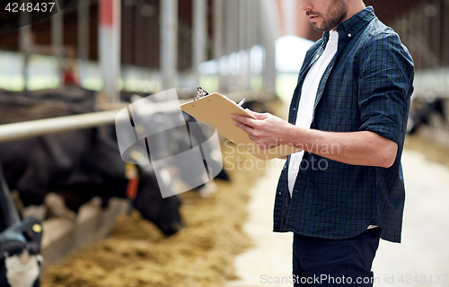 Image of farmer with clipboard and cows in cowshed on farm