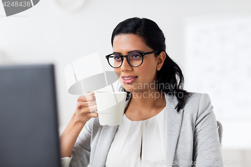 Image of businesswoman drinking coffee at office computer