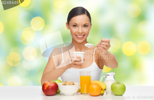 Image of happy woman with fruits, cereals eating yogurt