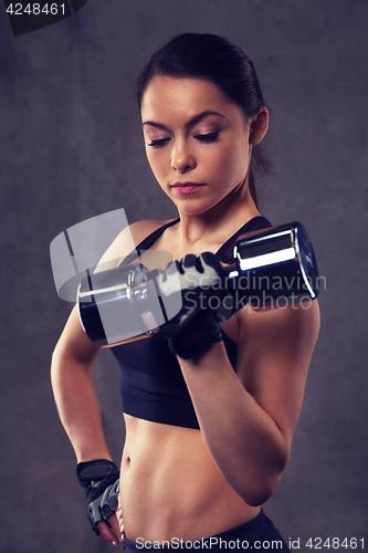 Image of young woman flexing muscles with dumbbells in gym