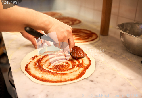 Image of cook applying tomato sauce to pizza at pizzeria