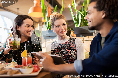 Image of happy friends eating and drinking at restaurant