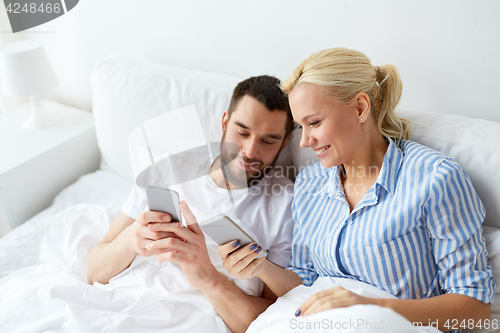 Image of happy couple with smartphones in bed at home