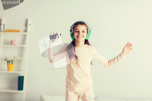 Image of girl jumping on bed with smartphone and headphones