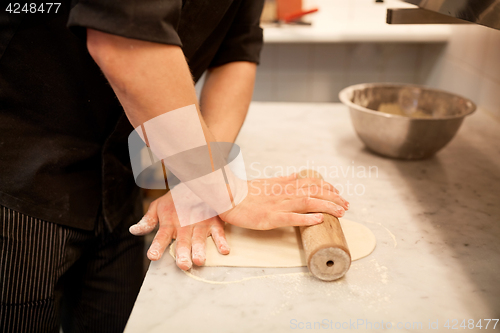 Image of chef with rolling-pin rolling dough at kitchen