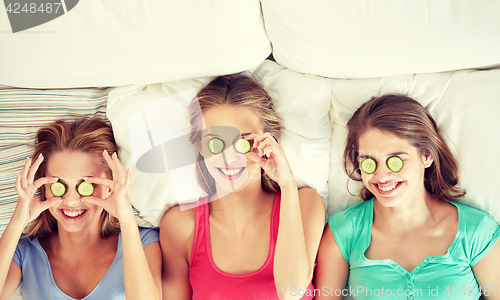 Image of happy young women with cucumber mask lying in bed