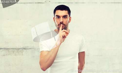 Image of young man making hush sign over gray wall