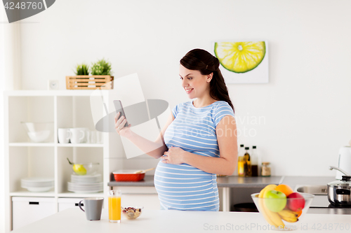 Image of happy pregnant woman with smartphone at kitchen